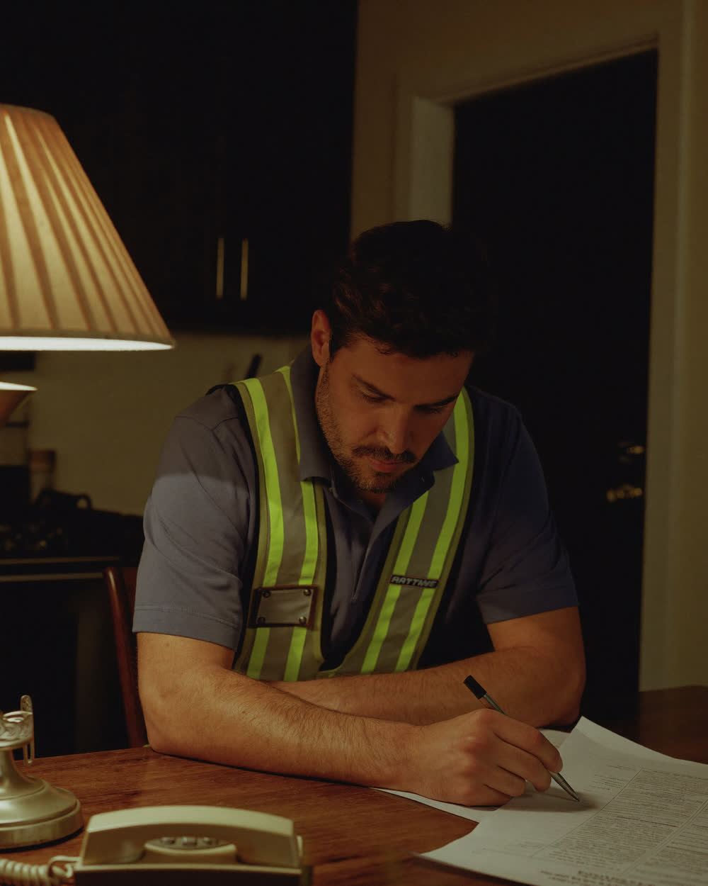A contractor sitting alone at his kitchen table in the evening with paperwork and a quiet phone